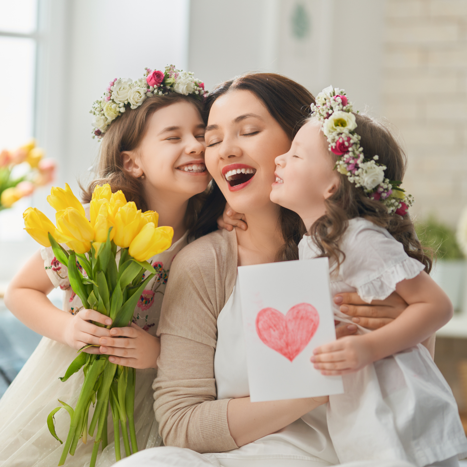 Two children hugging and kissing their mum while gifting a heart card and daffodils | Mother's Day - Clair de Lune UK