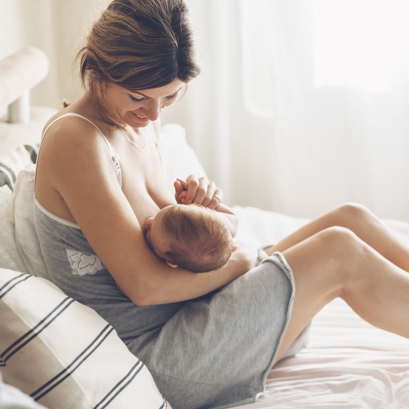 Mum sat on the bed recovering from a c-section breastfeeding her newborn - Clair de Lune UK