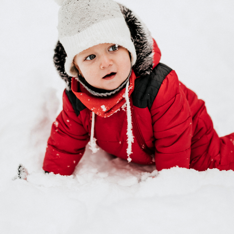 A boy toddler in a red snow suit playing in the snow | Family Christmas - Clair de Lune UK