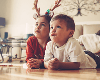 Two children dressed in Christmas jumpers and reindeer antlers lying on the floor watching Christmas films | Family Christmas - Clair de Lune UK