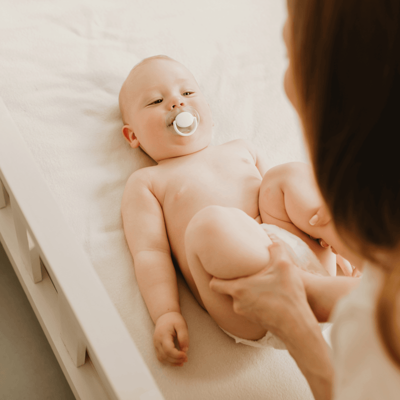 Toddler lying on a hospital bed sucking a dummy while the doctor moves their legs around to check for hip dysplasia - Clair de Lune UK