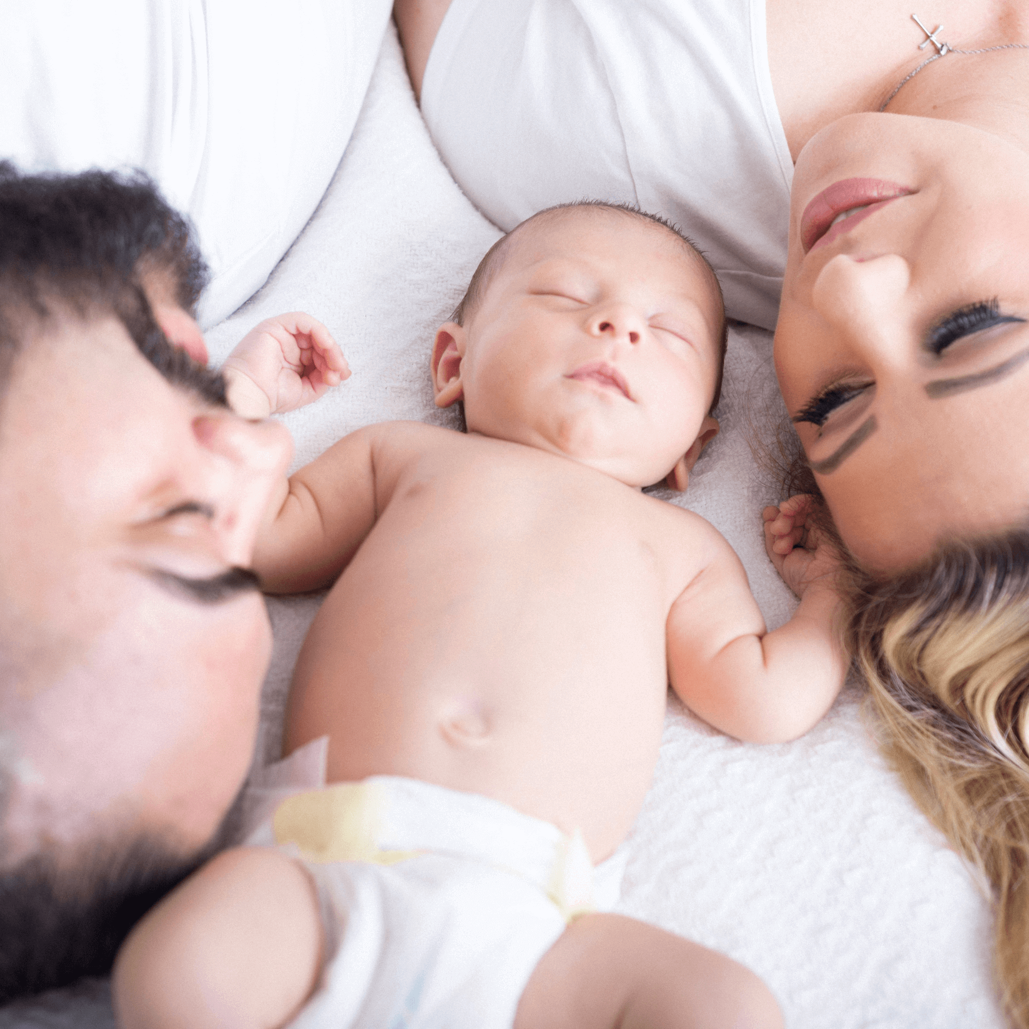 Mum and dad lying on the bed with their newborn baby | Parenting tips and advice - Clair de Lune UK