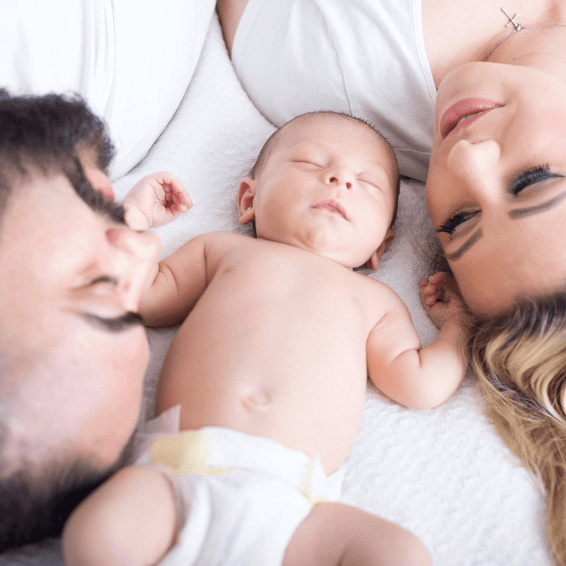 Mum and dad lying on the bed with their newborn baby | Parenting tips and advice - Clair de Lune UK
