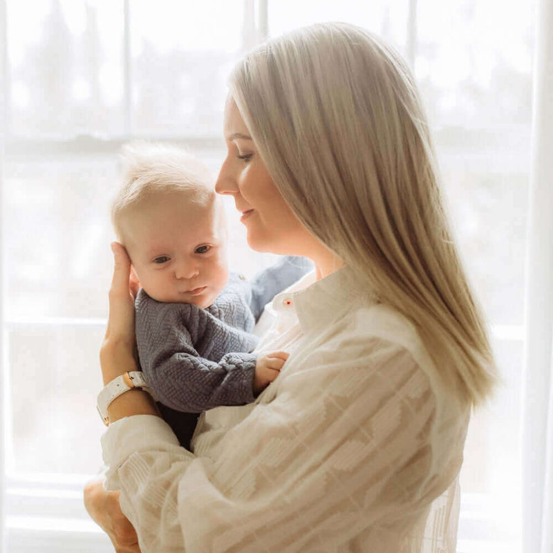 Mum holding her newborn baby boy in front of a light and airy window on Mother's Day | How to Celebrate Mother’s Day as a First-Time Mum - Clair de Lune UK