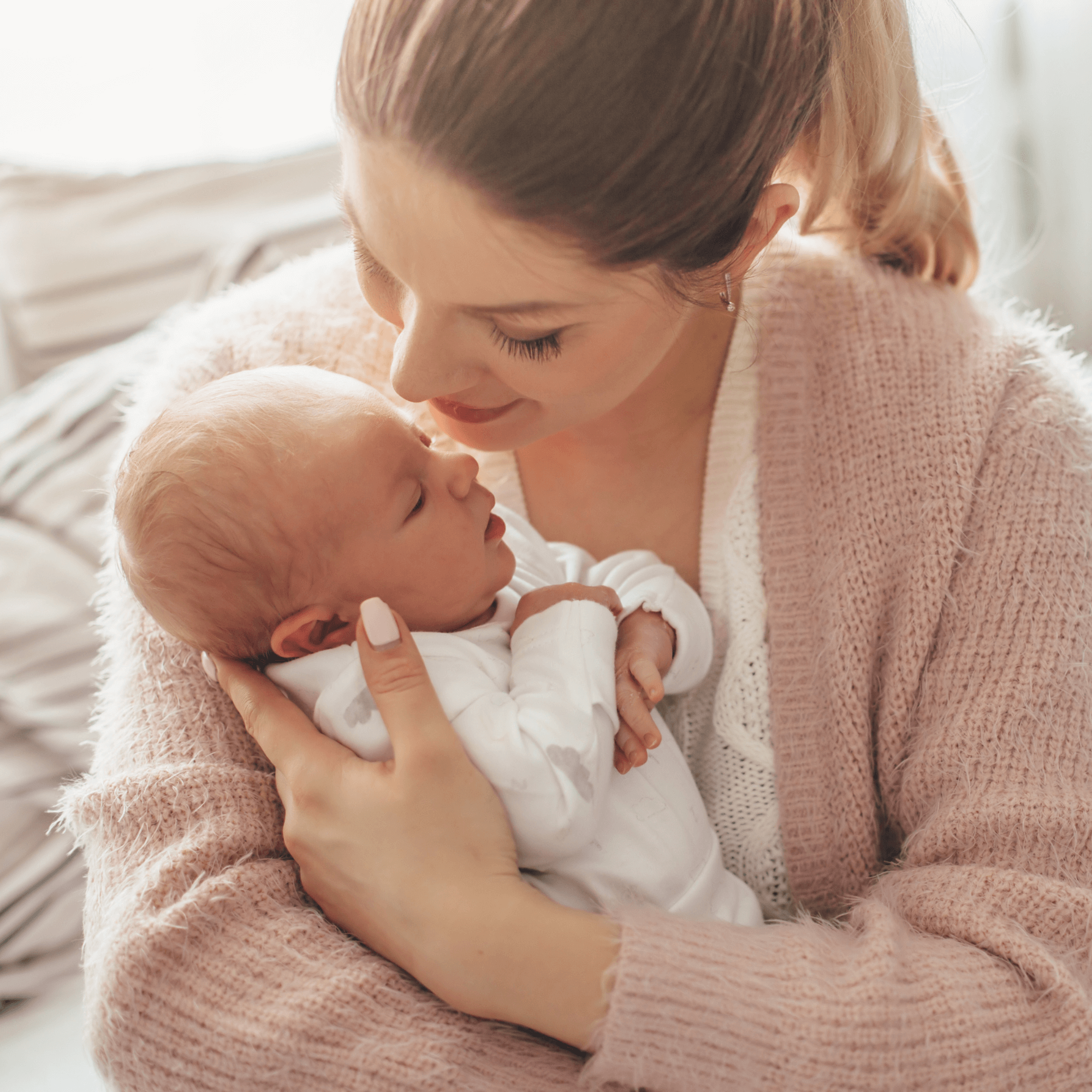 Mum with her hair tied back wearing a floaty pale pink cardigan staring into the eyes of her newborn that is swaddles in her arms | Family Time | Mother's Day - Clair de Lune UK