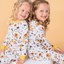 Two girls sitting back to back and smiling wearing the Grow Grows Organic Honey Bees Pyjamas | Organic Kids PJs and Nightwear - Clair de Lune UK