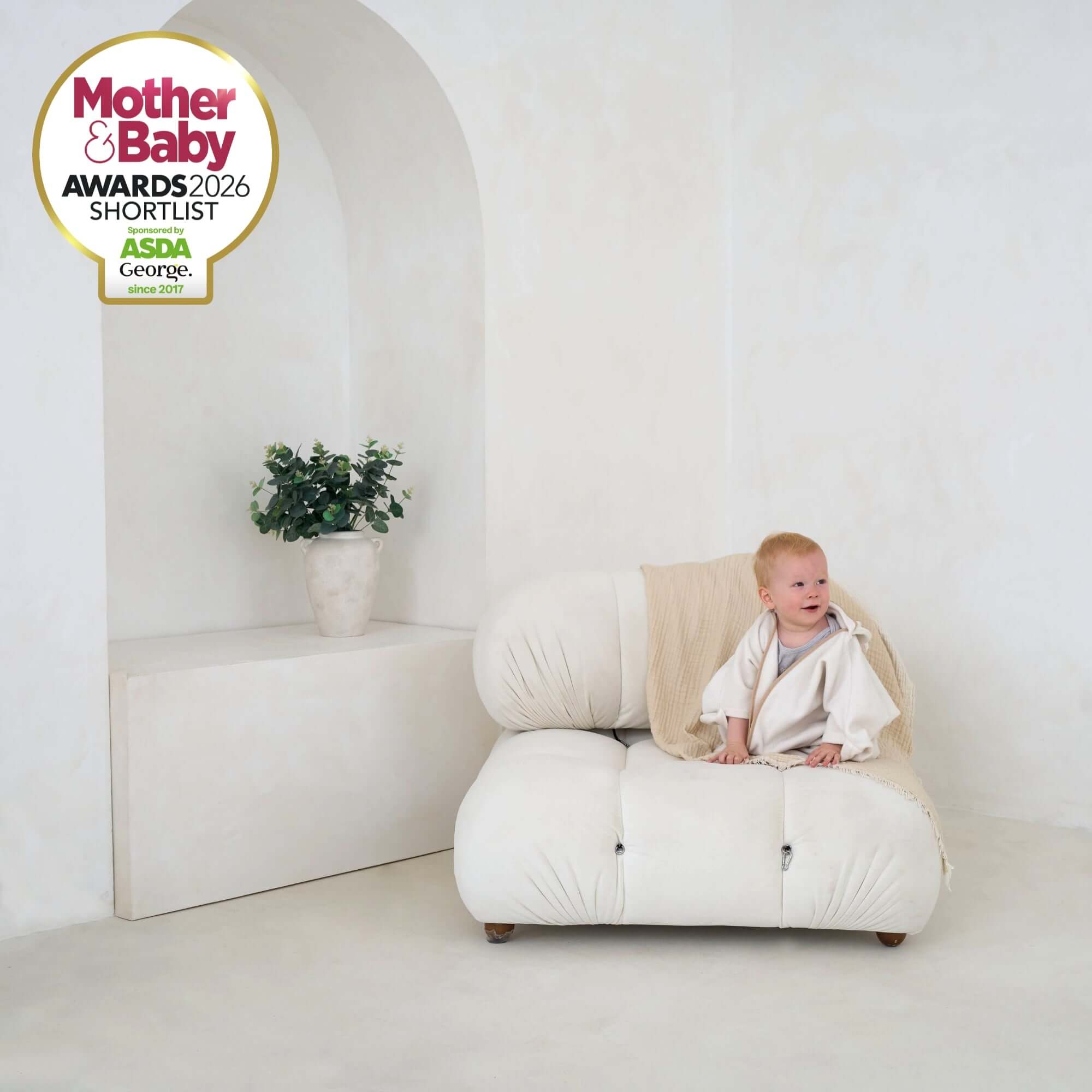 Toddler sitting on a white bean bag wearing Cream Star Fleece Baby Wrap Blanket for a winter walk - Mother & Baby Shortlist Award 2026 | Cosy Baby Blankets | Swaddle Blanket | Nursery Bedding - Clair de Lune UK