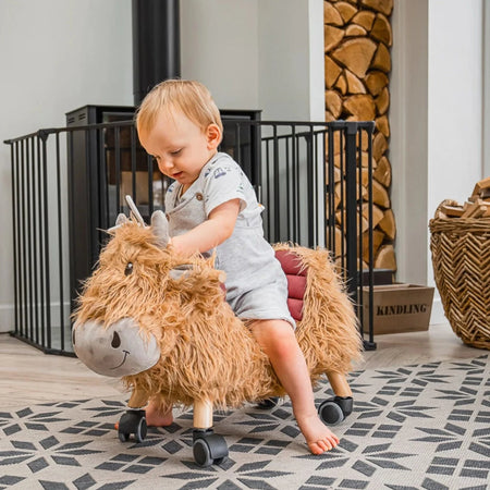 Toddler boy playing and riding on the Little Bird Told Me Hubert Highland Cow Ride On Toy helping improve his sensory skills | Baby Walkers and Ride On Toys | Montessori Activities For Babies & Kids | Toys | Baby Shower, Birthday & Christmas Gifts - Clair