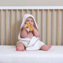 Baby in the Essentials cot bed wearing one of the Basic Hooded Towels in Biscuit | Baby Bathing & Changing Essentials - Clair de Lune UK