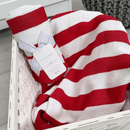 East Coast Silvercloud Candy Cane Wide Stripe Red and White baby blanket showing the tag and ribbon packaging rolled and draped on a chair | Cosy Baby Blankets | Swaddles and Receiving Blankets - Clair de Lune UK