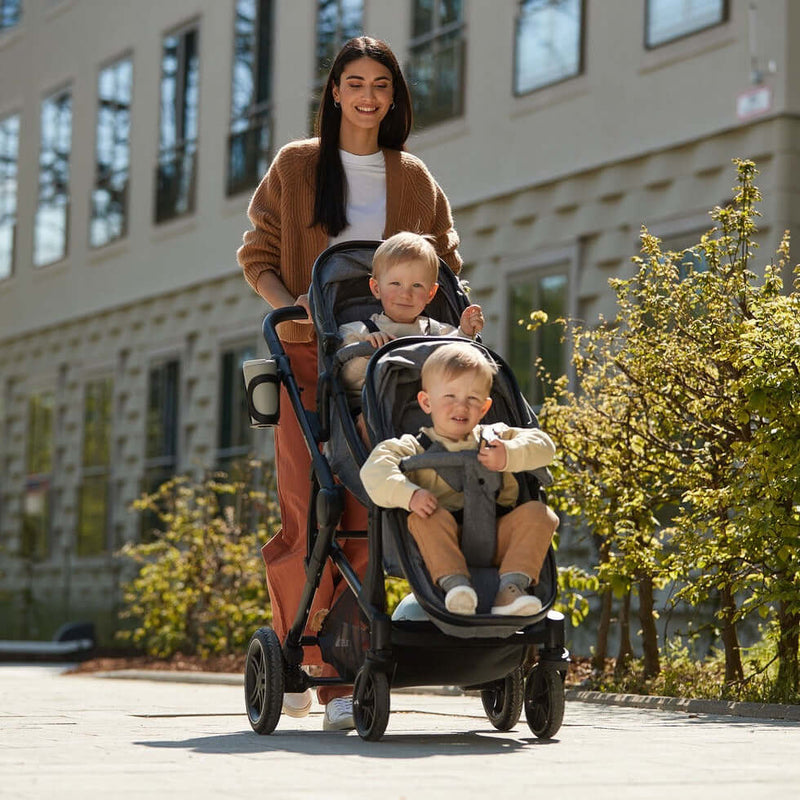 Mum pushing her Hauck Atlantic Twin Tandem Pushchair in the town centre with her twins sitting comfortably on the stroller | Strollers, Pushchairs & Prams | Baby Travel Essentials - Clair de Lune UK
