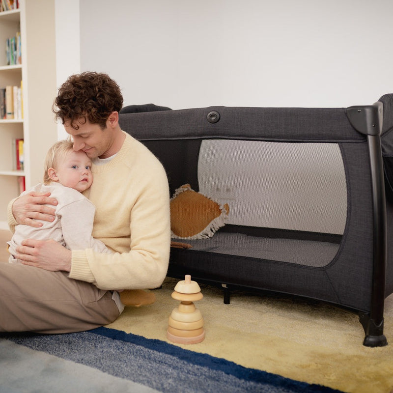 Dad hugging his child next to the Hauck Play N Relax Centre 4in1 Premium Travel Cot | Travel Cots & Travel Bassinets | Cots, Cot Beds, Toddler & Kid Beds | Nursery Furniture - Clair de Lune UK