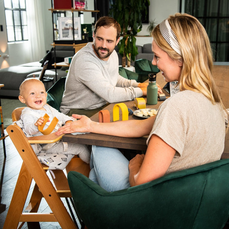 Mum and dad feeding toddler sitting on the Hauck Alpha+ Wooden Highchair with Removable Front Bar in Natural | Highchairs | Feeding & Weaning - Clair de Lune UK