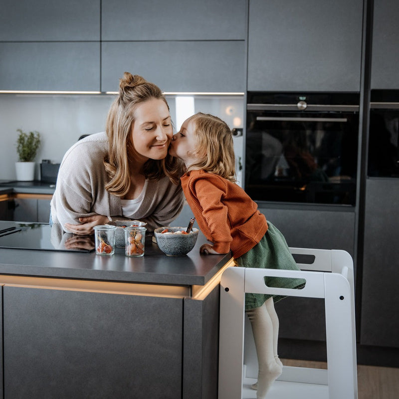Daughter joining cooking with her mum with the White Universal Hauck Learn N Explore Montessori Kitchen Helper & Learning Tower | Montessori Activities For Babies & Kids - Clair de Lune UK