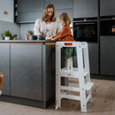 Toddler girl chopping a banana in the white Hauck Learn N Explore Learning Tower | Feeding & Weaning | Montessori Furniture For Babies & Toddlers - Clair de Lune UK