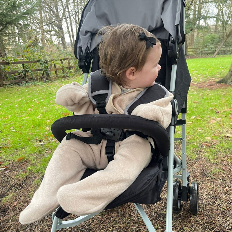 Toddler girl wearing the Beige Star Fleece Baby Wrap Blanket sitting on a black pushchair in a park | Cosy Baby Blankets | Nursery Bedding | Newborn, Baby and Toddler Essentials - Clair de Lune UK