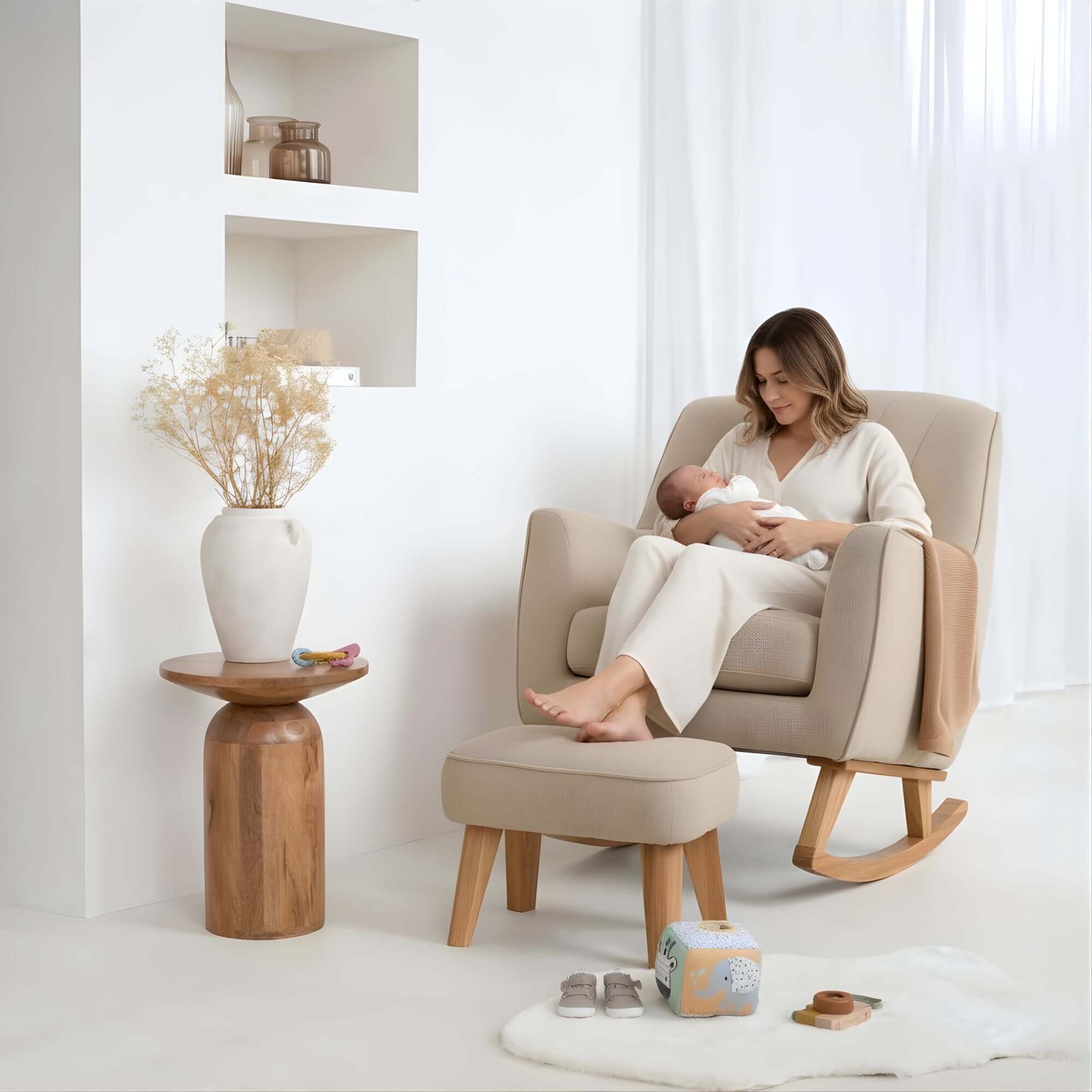 Mum cradling her newborn baby in the Cream Bouclé Rocking Chair and Footstool by a large window and play mat in a white nursery | Nursing Chair | Nursery Furniture - Clair de Lune UK