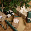 Little Dreamers Luxury Organic Swaddle Bag in brown packaging being wrapped by the Christmas tree in green wrapping paper | Baby Sleeping Bags | Organic Nursery Bedding | Baby's First Christmas Gifts - Clair de Lune UK