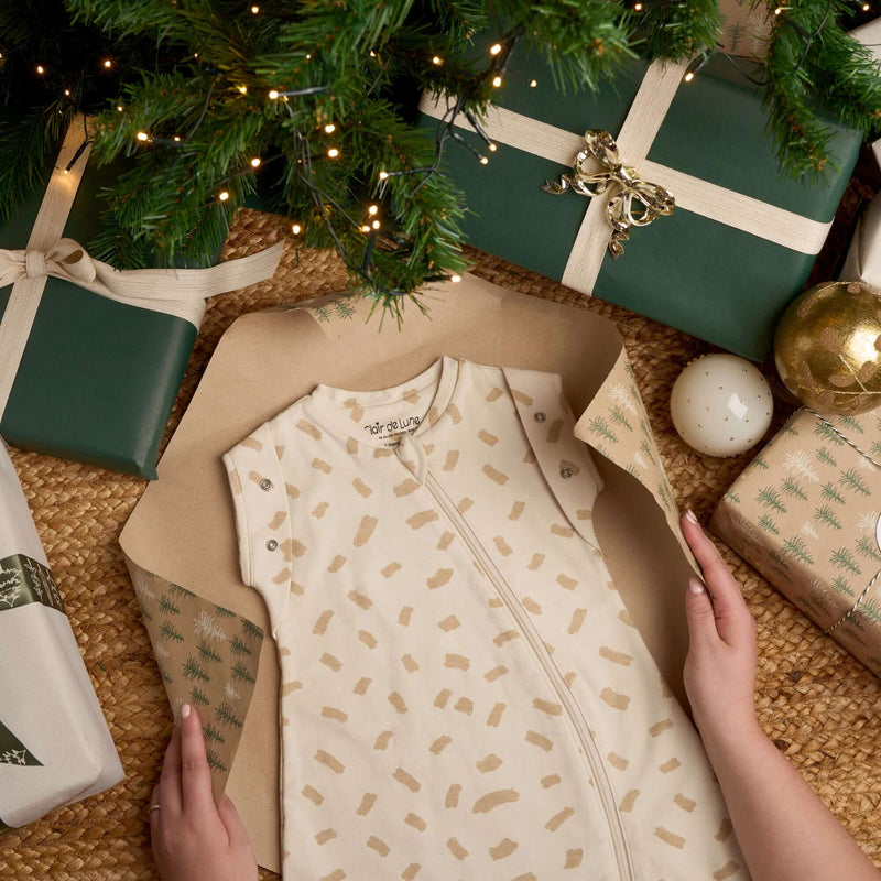 Little Dreamers Luxury Organic Swaddle Bag being unwrapped on Christmas morning surrounded by gorgeous green gifts | Baby Sleeping Bags | Organic Nursery Bedding | Baby's First Christmas Gifts - Clair de Lune UK