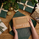 Person holding the biscuit organic cotton knitted blanket in beautiful brown box packaging under a decorated Christmas tree | Soft Baby Blankets | Organic Nursery Essentials | Baby's First Christmas - Clair de Lune UK