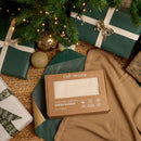 The cream organic cotton knitted blanket in beautiful brown box packaging under a decorated Christmas tree | Soft Baby Blankets | Organic Nursery Essentials | Baby's First Christmas - Clair de Lune UK