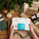 Jungle Dream Cot Bed Sheets being held under the Christmas tree with lots of wrapped gifts | Cot Bedding | Christmas Gifts for Baby and Toddler - Clair de Lune UK