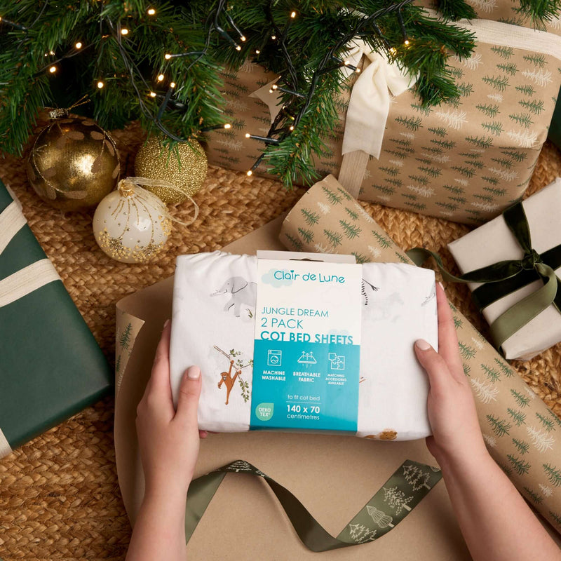 Jungle Dream Cot Bed Sheets being held under the Christmas tree with lots of wrapped gifts | Cot Bedding | Christmas Gifts for Baby and Toddler - Clair de Lune UK