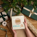 Person holding the Oatmeal Star Fleece baby wrap blanket box under a Christmas tree with wrapped gifts | Baby's First Christmas Gifts | Cosy Baby Blankets - Clair de Lune UK