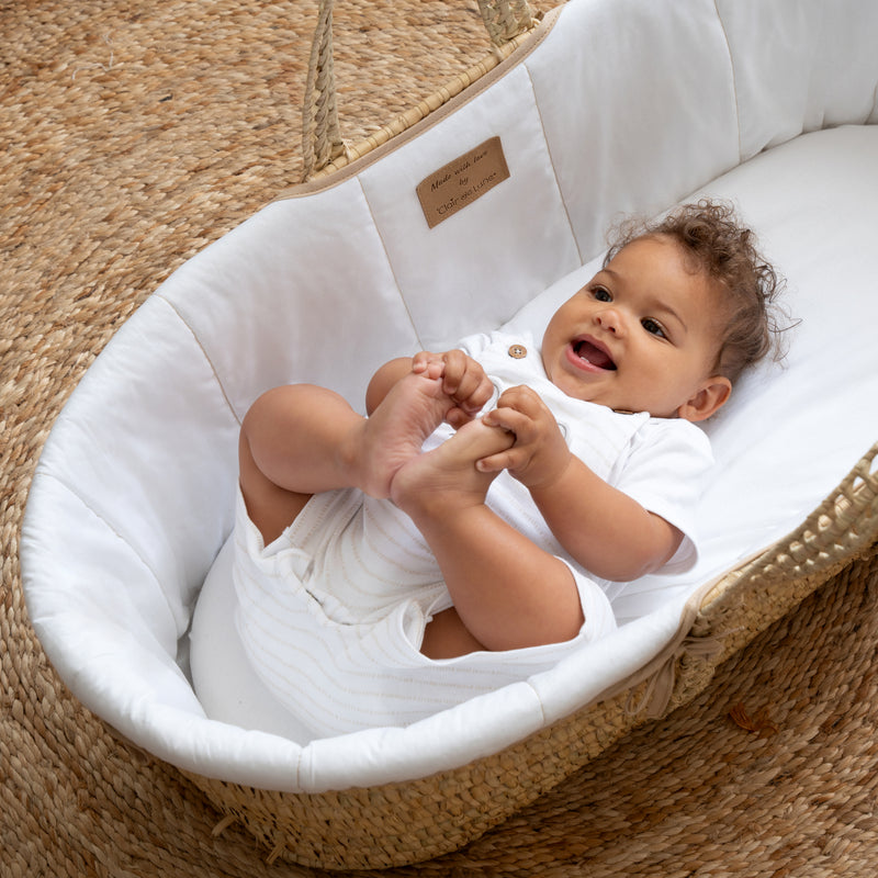 Baby boy smiling in the White Organic Palm Moses Basket on a natural brown rug | Moses Baskets | Co-sleepers | Nursery Furniture - Clair de Lune UK