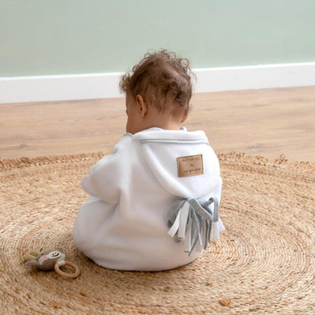 Baby sitting on the floor wearing the White Star Fleece Baby Wrap Blanket | Cosy Baby Blankets | Swaddles | Baby Christmas Gift 2024 - Clair de Lune UK