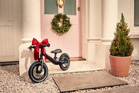 Bently Bike wrapped in a big red bow outside the front door with a christmas wreath and christmas tree | Childrens Toys & Gifts | Baby Christmas Gift 2024 - Clair de Lune UK