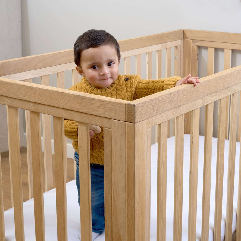 Baby playing inside the Oak Cot Bed in a Scandi Natural Nursery Room | Cots, Cot Beds, Toddler & Kid Beds | Nursery Furniture - Clair de Lune UK