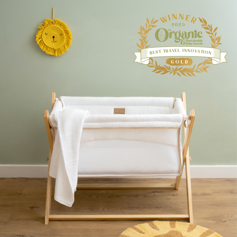 White Organic Folding Crib in front of a Scandi Sage Green wall with the Organic Baby Awards Gold Winner logo | Bedside & Folding Cribs | Next To Me Cots & Newborn Baby Beds | Co-sleepers - Clair de Lune UK