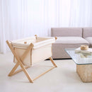 Cream Organic Folding Crib in a white stylish living room next to a grey corner sofa | Bedside & Folding Cribs | Co Sleeper & Travel Cots | Nursery Furniture - Clair de Lune UK
