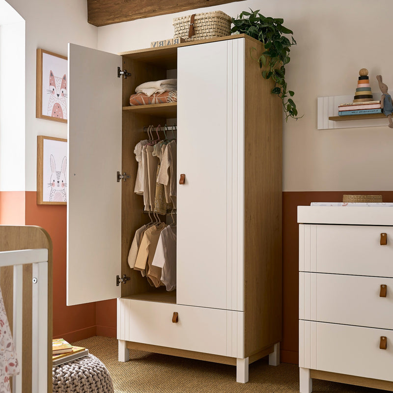 White and Natural CuddleCo Rafi Freestanding Double Wardrobe with Drawer in a dark orange nursery with full of baby clothes | Wardrobes & Shelves | Storage Solutions | Nursery Furniture - Clair de Lune UK 