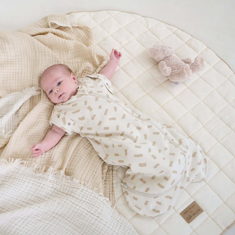 Newborn baby wearing Little Dreamers Luxury Organic Swaddle Bag lying on an organic play mat | Baby Swaddle Bag | Newborn Sleeping Bag | Nursery Bedding - Clair de Lune