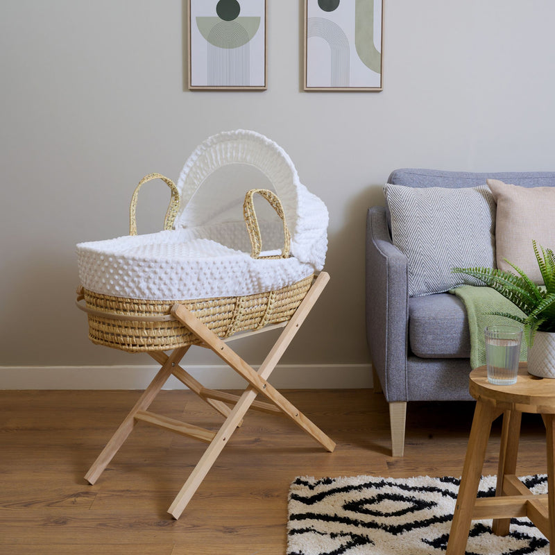 White Dimple Palm Moses Basket on a natural folding stand in a beige living room by the coffee table | Moses Basket Stand | Moses Baby Basket & Bassinet Accessories | Nursery Furniture - Clair de Lune UK