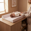 Mum tending to baby lying on the Brown Gingham Anti-Roll Wedge Baby Changing Mat on an oak changing unit but a bright window | Baby Bathing & Changing Essentials - Clair de Lune UK