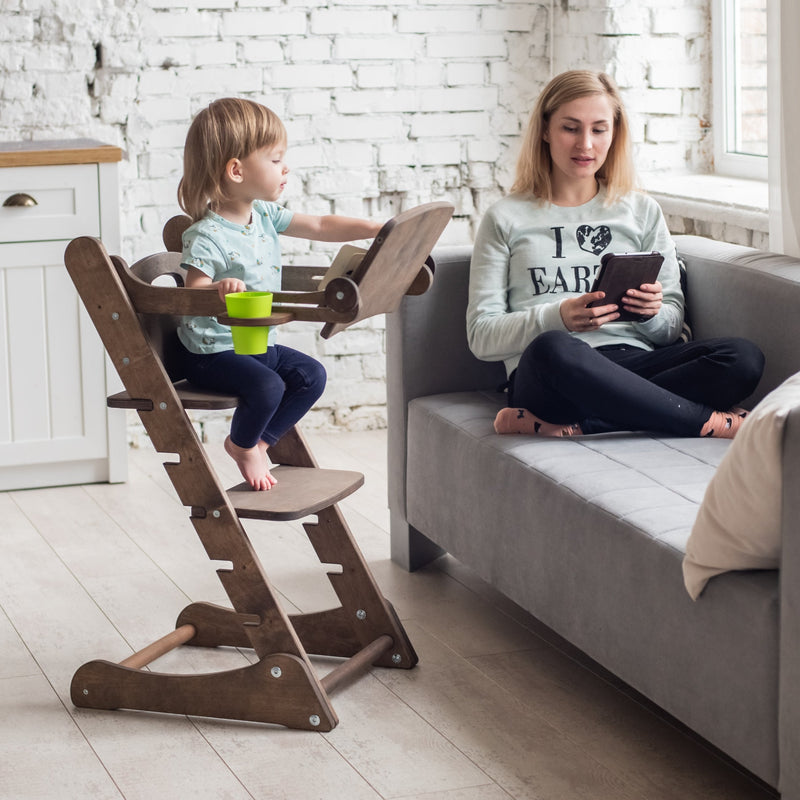 A girl reading books while sitting on the Chocolate Goodevas 3in1 Highchair with Adjustable Tabletop next to her mom | Highchairs | Feeding & Weaning - Clair de Lune UK