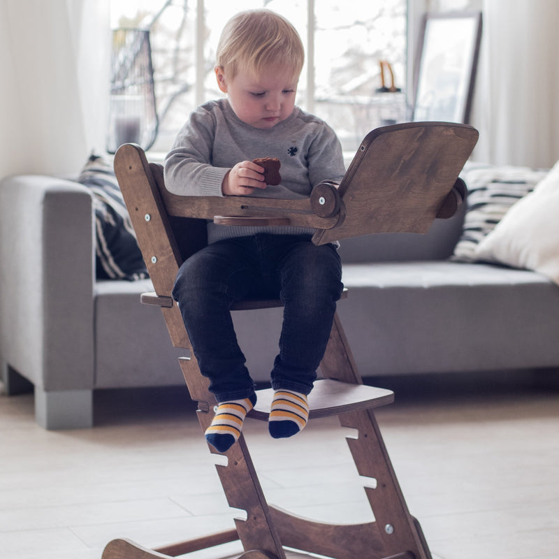 A boy eating his biscuit and reading books while sitting on the Chocolate Goodevas 3in1 Highchair with Adjustable Tabletop | Highchairs | Feeding & Weaning - Clair de Lune UK