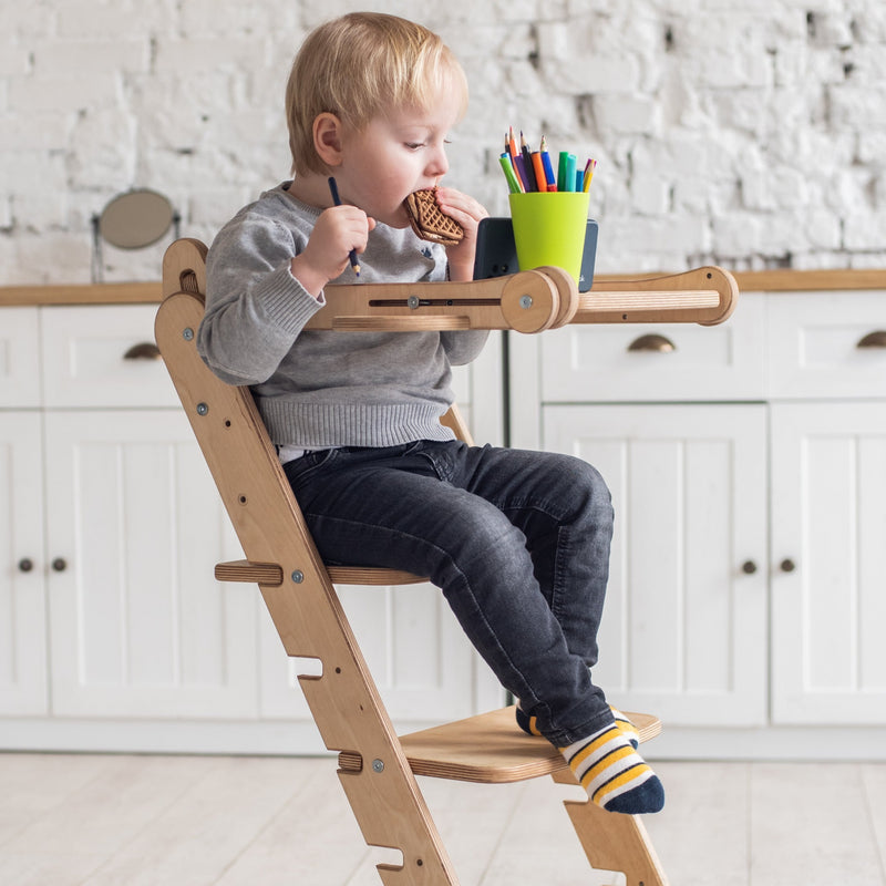 A boy eating his biscuit and reading books while sitting on the Natural Goodevas 3in1 Highchair with Adjustable Tabletop | Highchairs | Feeding & Weaning - Clair de Lune UK
