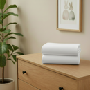 White 2 pack pram/crib fitted sheets folded on a chest of drawers in a beige nursery | Soft Baby Sheets | Crib Bedding - Clair de Lune UK
