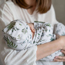 A close-up lifestyle shot of a mother holding her baby who is wearing a matching GrowGrows sleepsuit, baby hat and baby bib