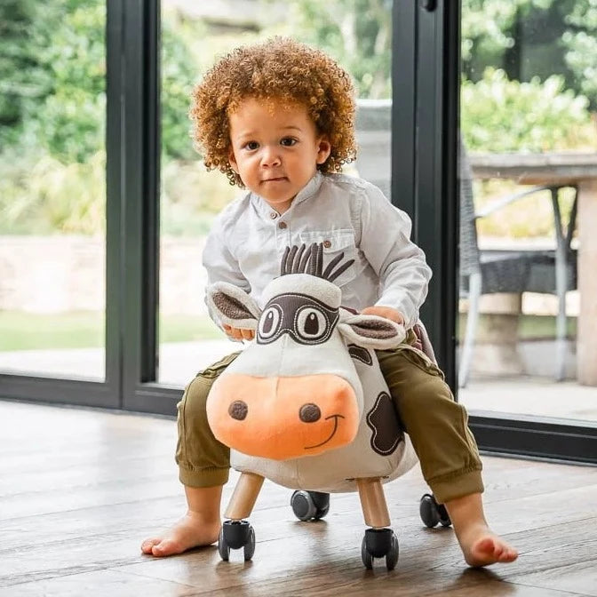 Little boy having fun racing the Little Bird Told Me Moobert Cow Ride On Toy around the house | Baby Walkers and Ride On Toys | Montessori Activities For Babies & Kids | Toys | Baby Shower, Birthday & Christmas Gifts - Clair de Lune UK