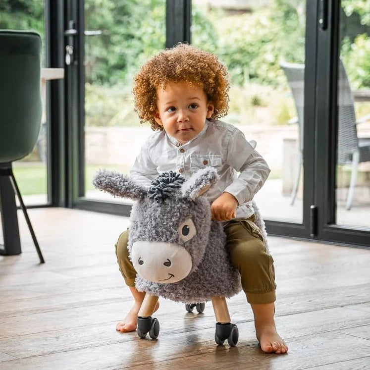 Boy riding his Little Bird Told Me Bojangles Donkey Ride On Toy in a dark green glass living room | Baby Walkers and Ride On Toys in a dark green | Montessori Activities For Babies & Kids | Toys | Baby Shower, Birthday & Christmas Gifts - Clair de Lune UK