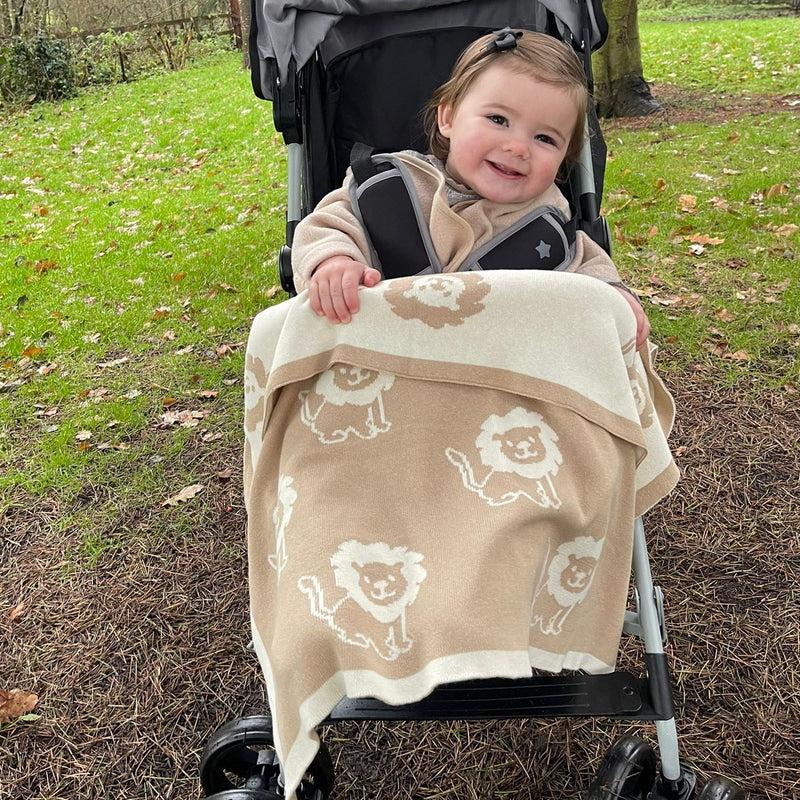 Baby smiling while wearing the Reversible Lion Knitted Blanket on her pushchair | Cosy Baby Blankets | Nursery Bedding | Newborn, Baby and Toddler Essentials - Clair de Lune UK