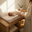 Mum tending to her baby on the Duckling Anti-Roll Wedge Baby Changing Mat with large oak changing unit by a bright window | Baby Bath Time Essentials - Clair de Lune UK