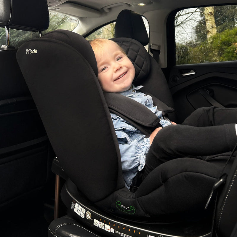 Smiling baby sitting on the My Babiie Billie Faiers iSize Quilted Black Spin Car Seat (40-150cm) | Baby, Toddler & Kid Car Seats | Travel With Baby - Clair de Lune UK