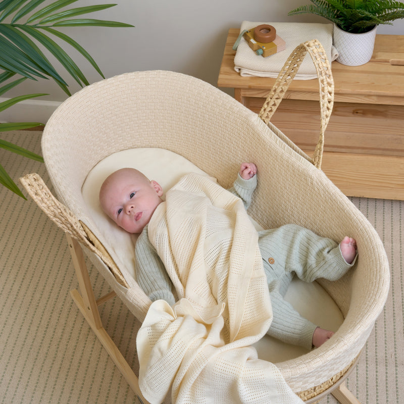 Baby cuddling the cream organic blanket lying in the Cream Organic Knitted Palm Moses Basket | Moses Baby Baskets, Bassinets | Organic Baby Essentials | Nursery Furniture - Clair de Lune UK