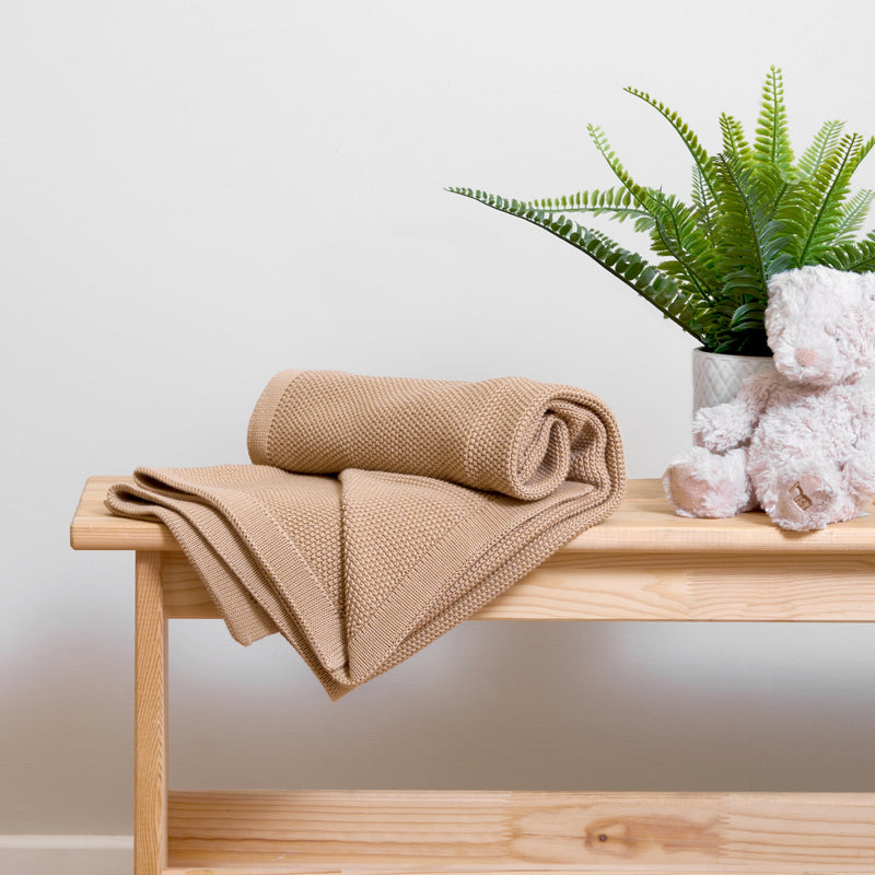 Biscuit brown Organic Knitted Baby Blanket rolled on an oak table in a neutral beige nursery | Cosy Baby Blankets & Swaddles | Nursery Bedding | Newborn Baby Essentials - Clair de Lune UK